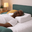 Homem idoso dormindo de costas em cama confortável, utilizando travesseiro cervical ortopédico branco com apoio adequado para o pescoço.